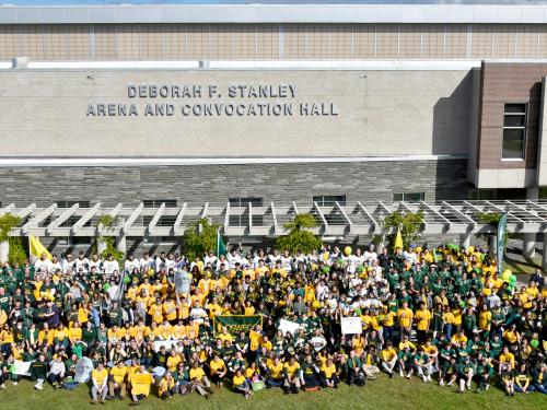 Many members of the Oswego family pose in front of the new sign for the Deborah F. Stanley arena and convocation hall for the 2021 Green and Gold Day photo