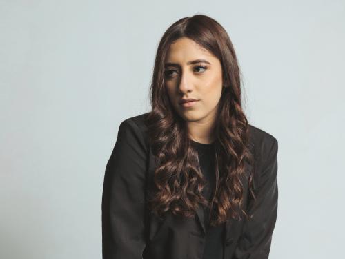 SUNY Oswego student Isanere Nunez poses for a professional photo in front of a light blue background.