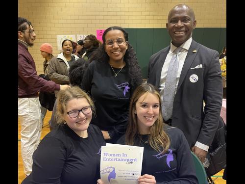 Student executive board members of the Women In Entertainment Club pose for a photo with President Nwosu at their Student Involvement Fair table.