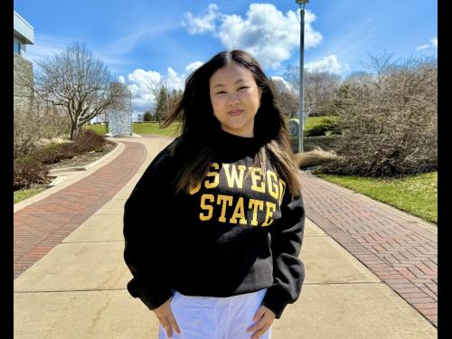 SUNY Oswego student Michelle Lau stands on campus in an black "Oswego State" sweatshirt.