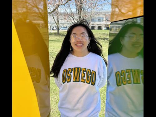 SUNY Oswego student Emma Halsey stands inside the green and gold "O" statue on SUNY Oswego's campus.