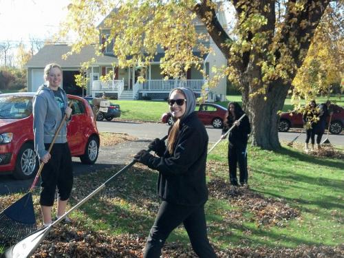 Student-athletes collecting leaves in a front yard