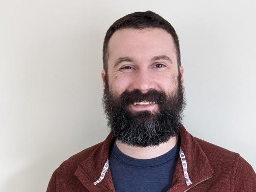 Headshot of Remmington Johnson wearing a maroon button up. Remmington has dark brown hair that is salt and pepper with a beard