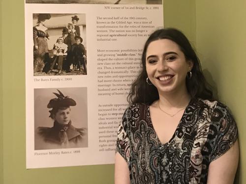 SUNY Oswego recent graduate Gabrielle Belmont stands next to her curated exhibit at the Richardson-Bates House Museum