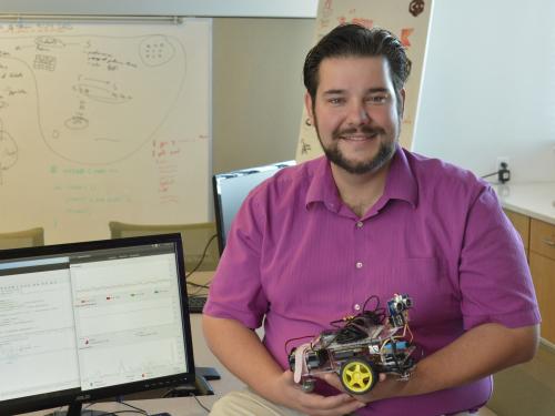 Computer science faculty member Bastian Tenbergen holds a small robotic car in his office