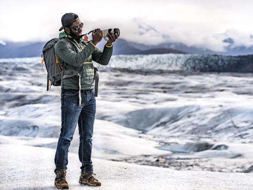 Mic-Anthony Hay looks through a camera with an arctic scene in background