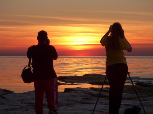 Two students take picture of an Oswego orange sunset over Lake Ontario