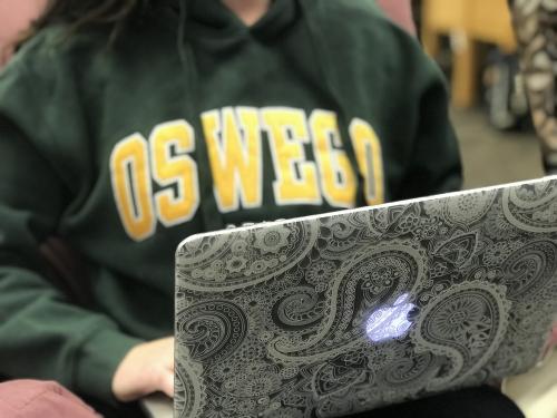 Student with an Oswego hoodie using a laptop computer