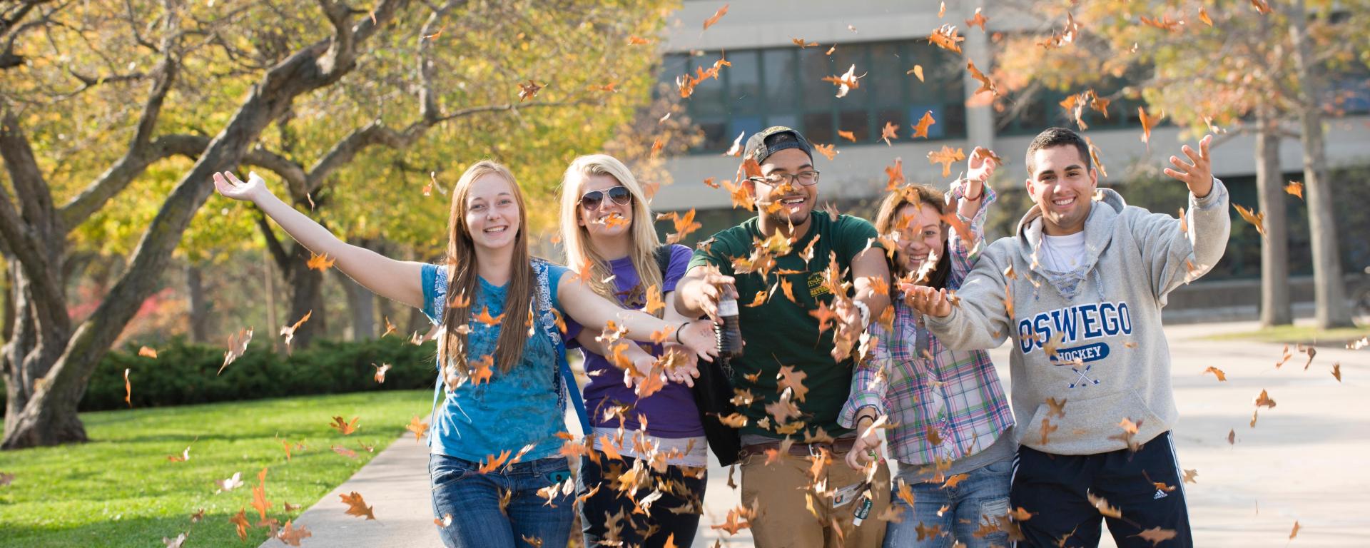A group of students outside, smiling and throwing leaves in the air