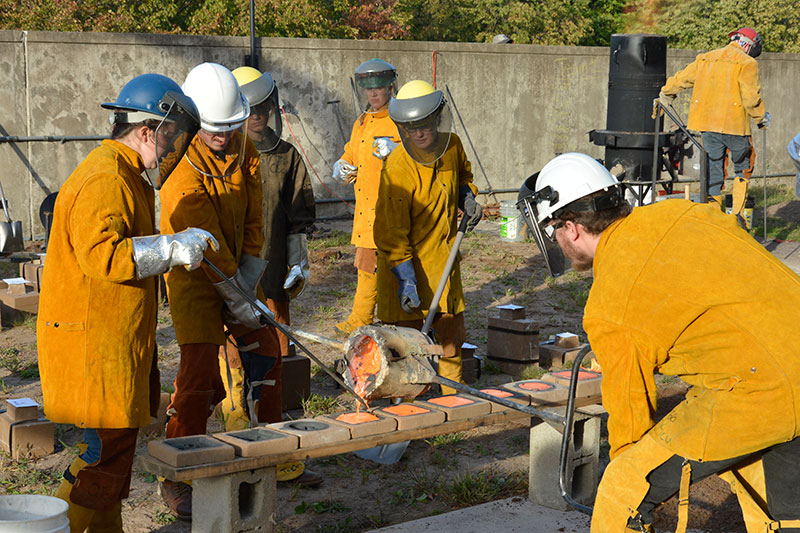 Student pour iron while wearing yellow protective suits and shielded helmets