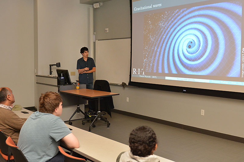 Daniel Wysocki speaks with a graphic related to gravitational waves in background