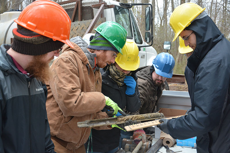 Faculty member Justin Stroup with students inspecting rock sediment core