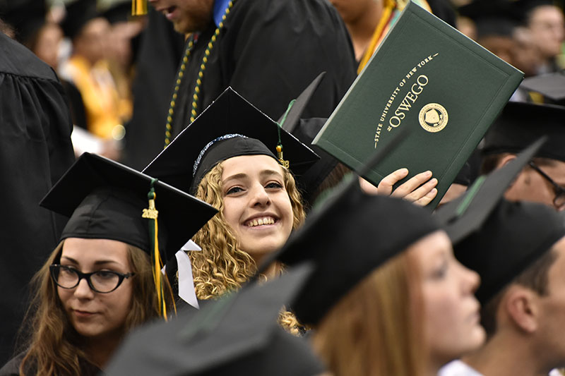 Student holds up her diploma booklet toward loved ones in audience