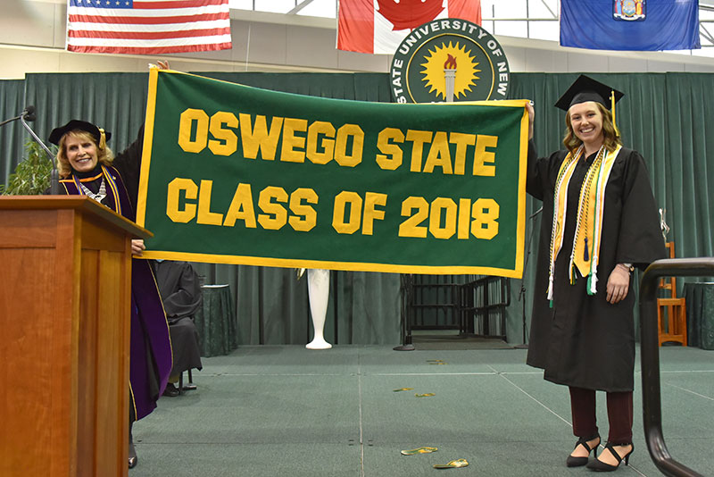 Alumni banner presenter Katherine Knopp (right) joins President Deborah F. Stanley hold up Class of 2018 banner