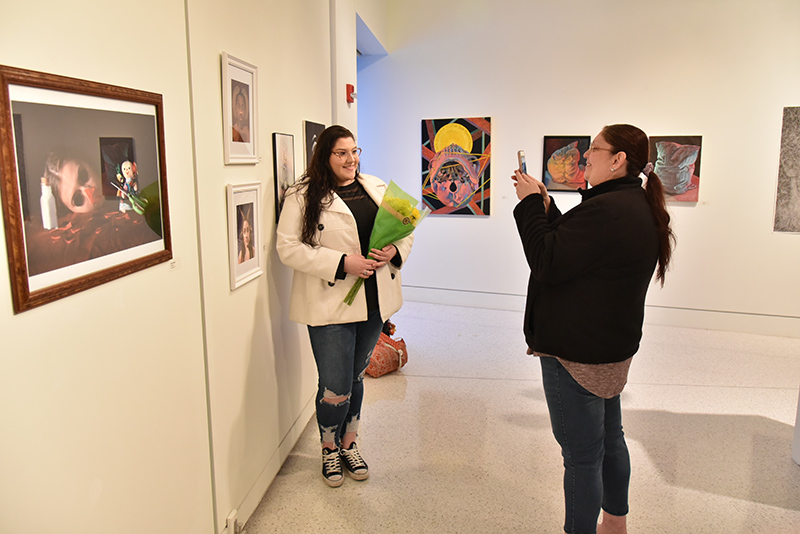 Arialees Alicea, a senior graphic design and Spanish dual major, poses with two of her astrology-themed digital design work in opening of 57th annual Juried Student Art Exhibition in Tyler Art Gallery