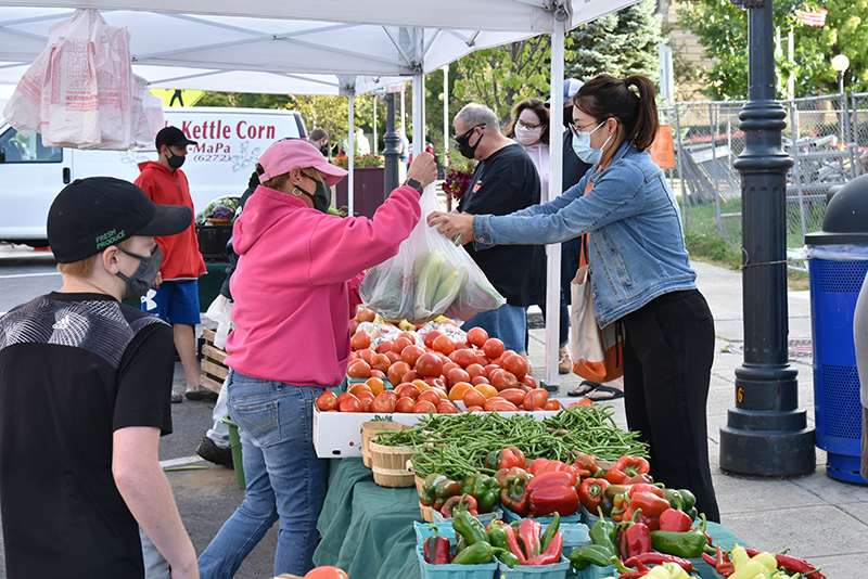 Renqian Yang, an art department faculty member who teaches ceramics, buys some locally-grown fresh produce Sept, 17 from Ingersoll Farms from Fulton at the Oswego Farmer's market on West First Street.