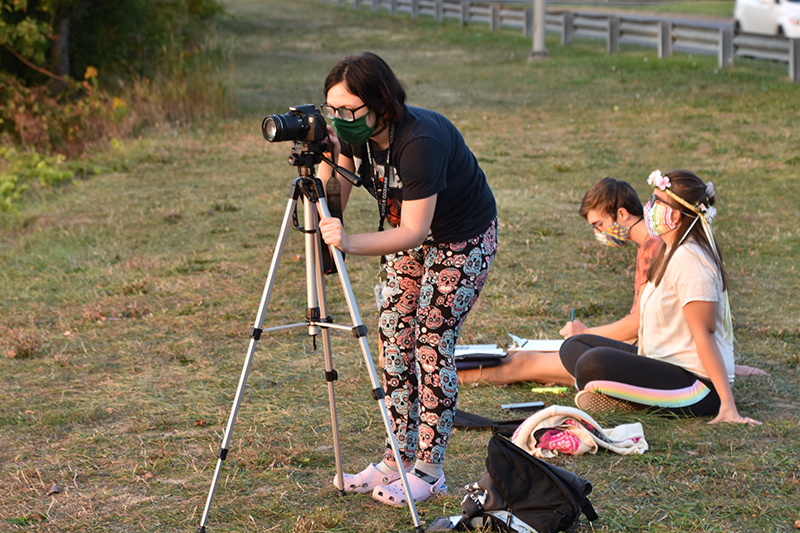 Payton Beauregard, a junior graphic design major, experiments with various camera settings for her “Intro to Photography” class while making sunset photographs near Seneca Hall. At right are Caysie Schrader, a sophomore creative writing major, and Michael Cinelli, a sophomore geology major, enjoying the sunset while working with a laptop computer.