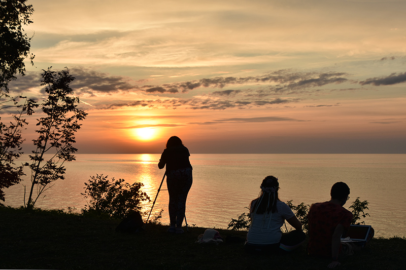 Students Payton Beauregard, Caysie Schrader and Michael Cinelli -- shown in an earlier photo setting up for the sunset -- get their majestic payoff over Lake Ontario.