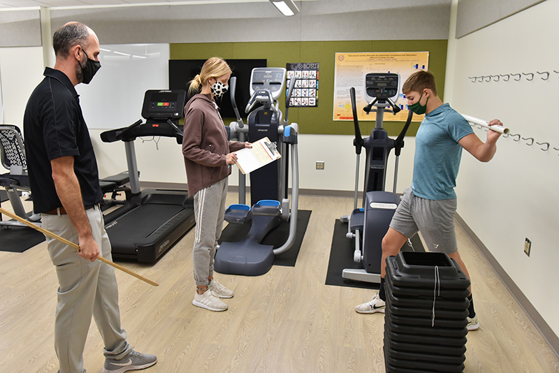 Griffin Biviano (right), a freshman health and wellness major, and Peyton Daeffler, a sophomore wellness management and nutrition major, work in the “Intro to Personal Training” class taught by Brian Wallace (left) in the Wellness Lab in the basement of Wilber Hall.