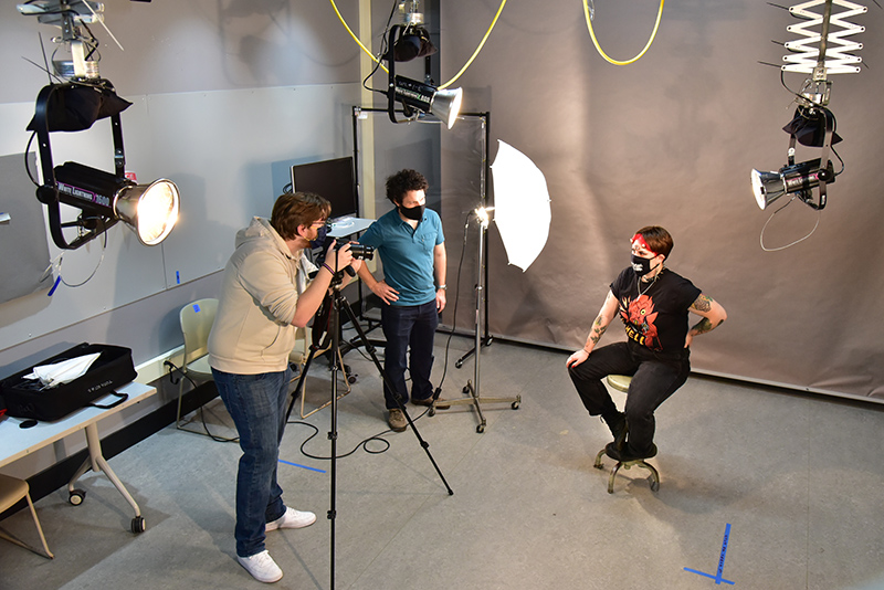 Patrick Higgins, a junior graphic design major, sets up a studio portrait in Tyler Hall's art photography studio of Kayli Clubine, a senior studio art major, during a “Digital Photography” class with art faculty member Peter Cardone (center).