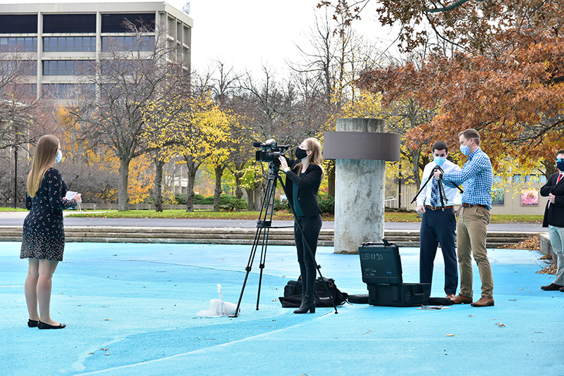 Stephanie Shtoyko (far left), a senior broadcasting and mass communications major, practices an on-camera news segment as Megan Trubia, a junior broadcasting and mass communications major, records her during a “Broadcast News Reporting” class taught by Michael Riecke, at right mentoring students in the class.