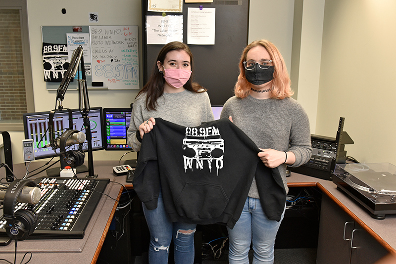 The approaching end of the semester means the passing of the mantle (or sweater) for a variety of organizations, including student-run WNYO FM 88.9 radio, which returned to in-studio shows for the campus and community. Incoming general manager Abigail Connolly (left) receives a welcome from Jenn Robilotto, the outgoing GM and a graduating senior.