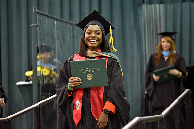 Blessed Sampa, who earned her MBA and bachelor's degrees, flashes a joyful smile displaying her diploma May 14 as she walks across the commencement platform in Marano Campus Center.