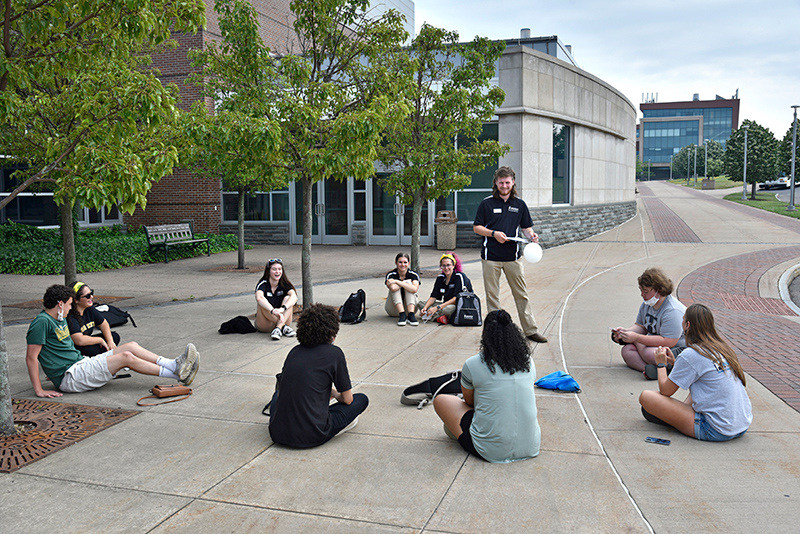 Laker Leader Ryan Parrish (standing) helps lead an orientation group on July 6 near the benches outside Marano Campus Center with fellow Laker Leaders, from left, Isabelle Keefe (white rim sunglasses), Rebekah Frank and Abby Lashinsky.