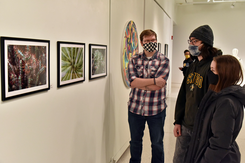 Patrick Higgins, left, a senior graphic design major, with friends William Rogers, a senior graphic design major; and Brittney Fahnestock, a freshman adolescence education and mathematics major, look at Higgins' photography artwork on display during a reception Feb. 11 for the 59th Annual Juried Student Art Exhibition in Tyler Art Gallery.