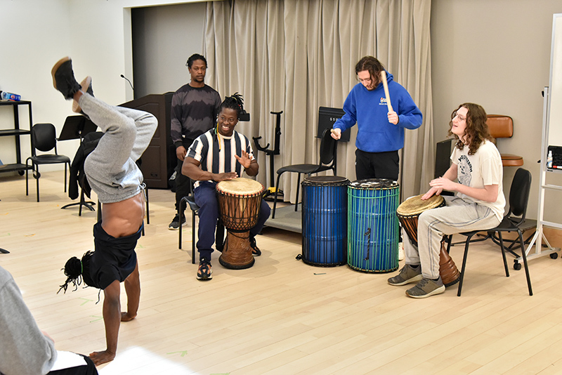 Several members of Cirque Kalabante gave a lively workshop in Tyler Hall on March 24 for an introduction to African dance and drumming. Students Ryan Peterson (blue shirt), a senior history major, and Angelo Antonelli (right), a sophomore audio recording production major, participate in a fast-paced percussion set as a troupe member dances in an unique acrobatic style. Cirque Kalabante performed in Waterman Theater to a sold-out crowd March 25.