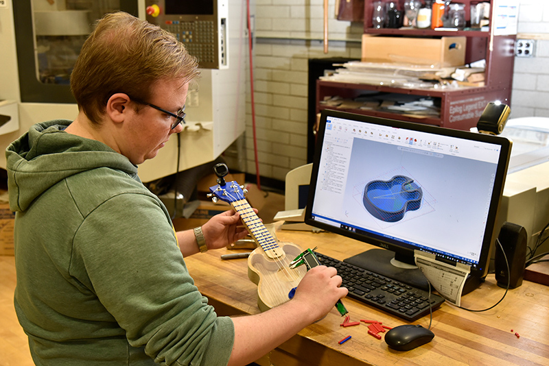 Technology education graduate student Jake Folts designed and constructed a stringed musical instrument from raw materials in a project over the spring semester. Pictured working in a Park Hall technology lab, he compares physical measurements to his CAD schematic.