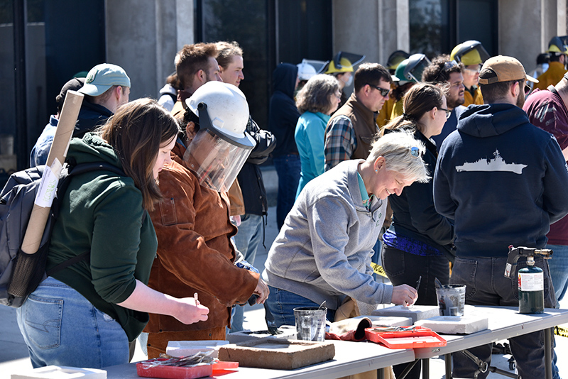 SUNY Oswego Officer in Charge Mary Toale creates an artistic design in a sand mold to be used in making a cast iron sculpture. Visitors to the Iron Pour on April 22 created unique designs during the annual collaborative event with art department and technology education students.