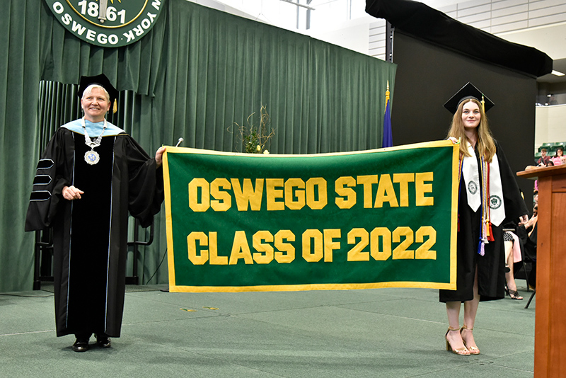 Graduate Jessica Burnett presents the Alumni Banner with SUNY Oswego's Officer in Charge Mary Toale during the School of Communication, Media and the Arts and School of Education commencement ceremony.