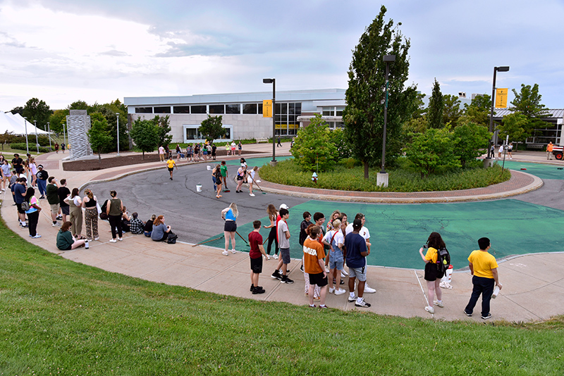 Students waiting to paint the Marano Campus Circle green with some sections still waiting to be painted