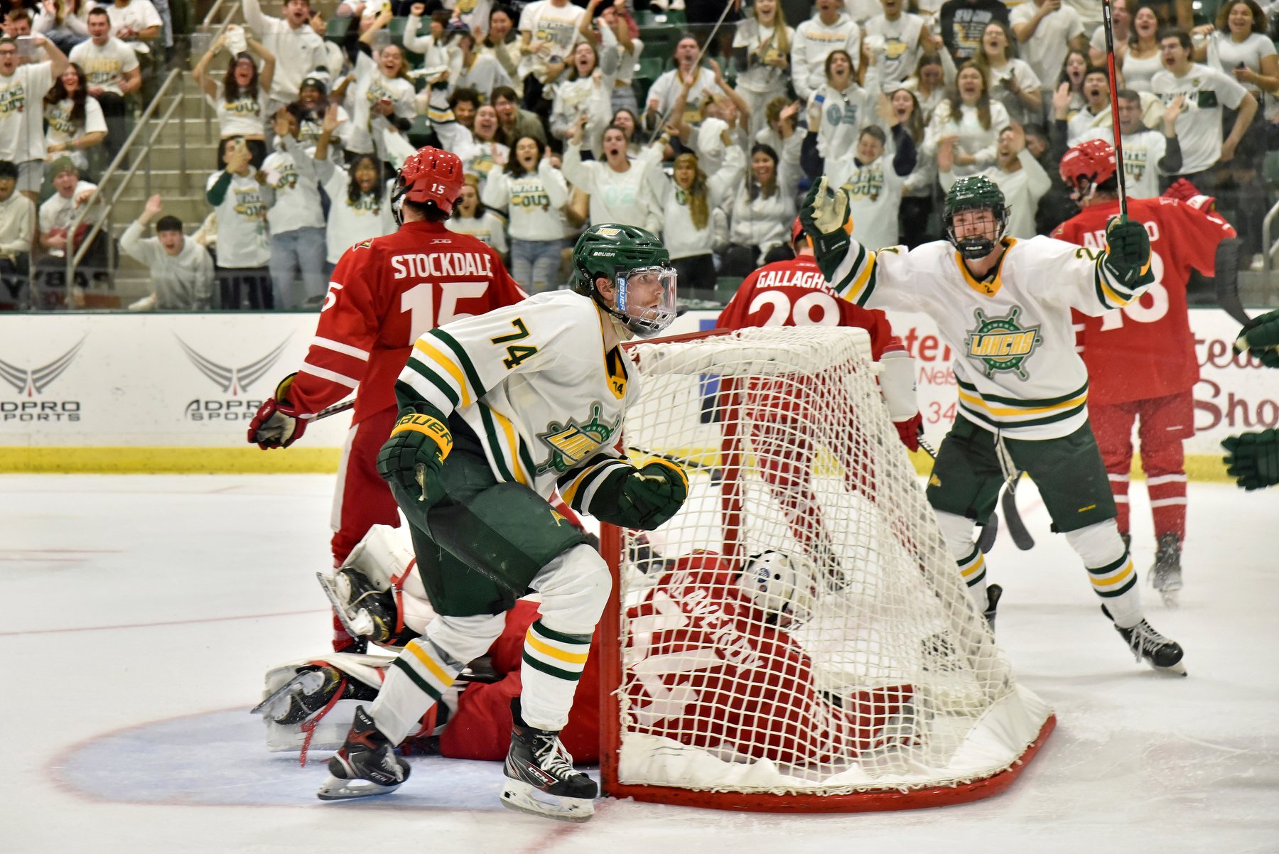 Ryan Dickinson (foreground #74), a junior defenseman, skates past the net after making the Lakers; fourth goal in 3rd period action accompanied by cheers from freshman forward Matt McQuade (#21, pictured), who scored Oswego's first goal in the game, along with the Oswego audience.