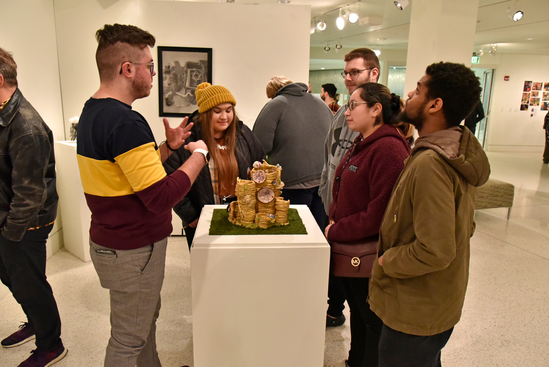 Isaiah Allen, left, talks with some friends about his art pieces during the Dec. 2 reception for the Bachelor of Fine Arts Exhibition held in Tyler Art Gallery. His ceramic piece (pictured) is titled "Mushrooms with Lady Bugs and Frogs." 