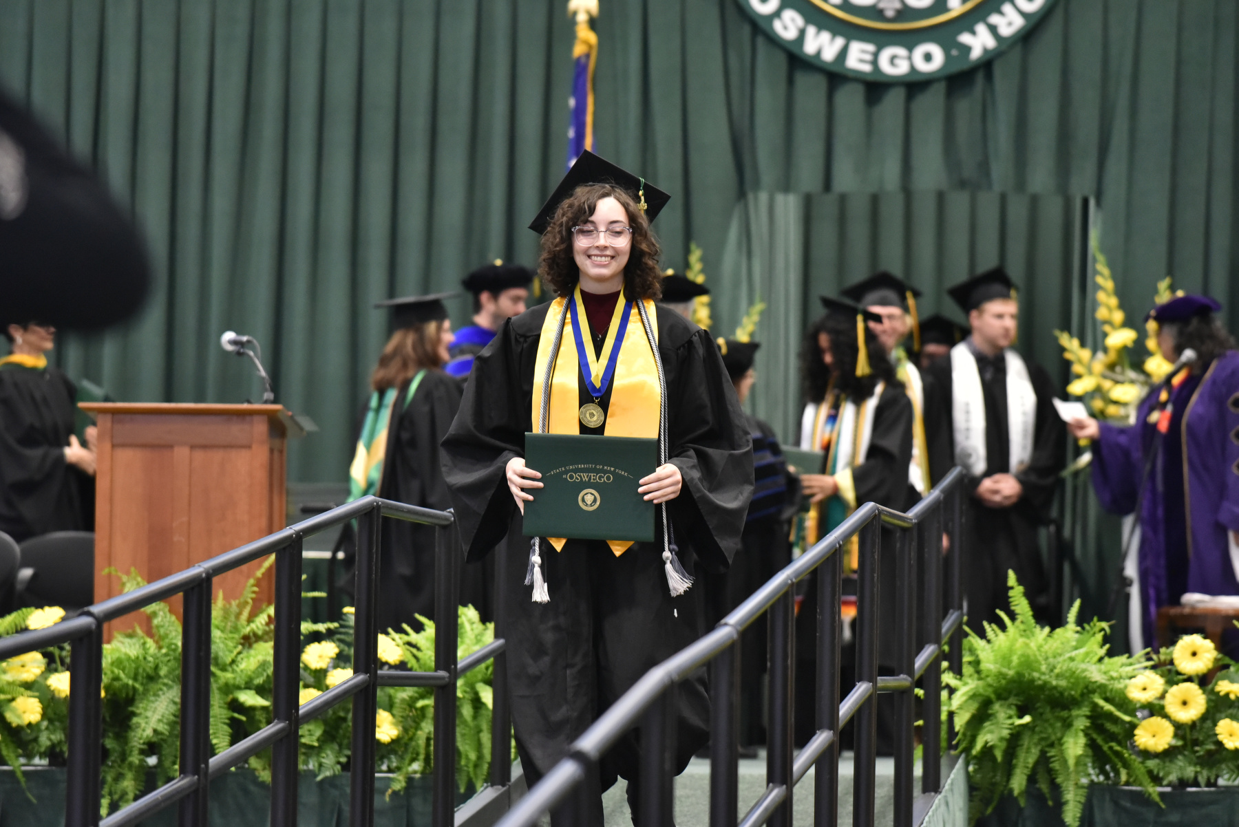 Brooke Goodman, a recipient of the 2023 Chancellor's Award for Student Excellence, walks across the platform at her commencement ceremony for the College of Liberal Arts and Sciences.