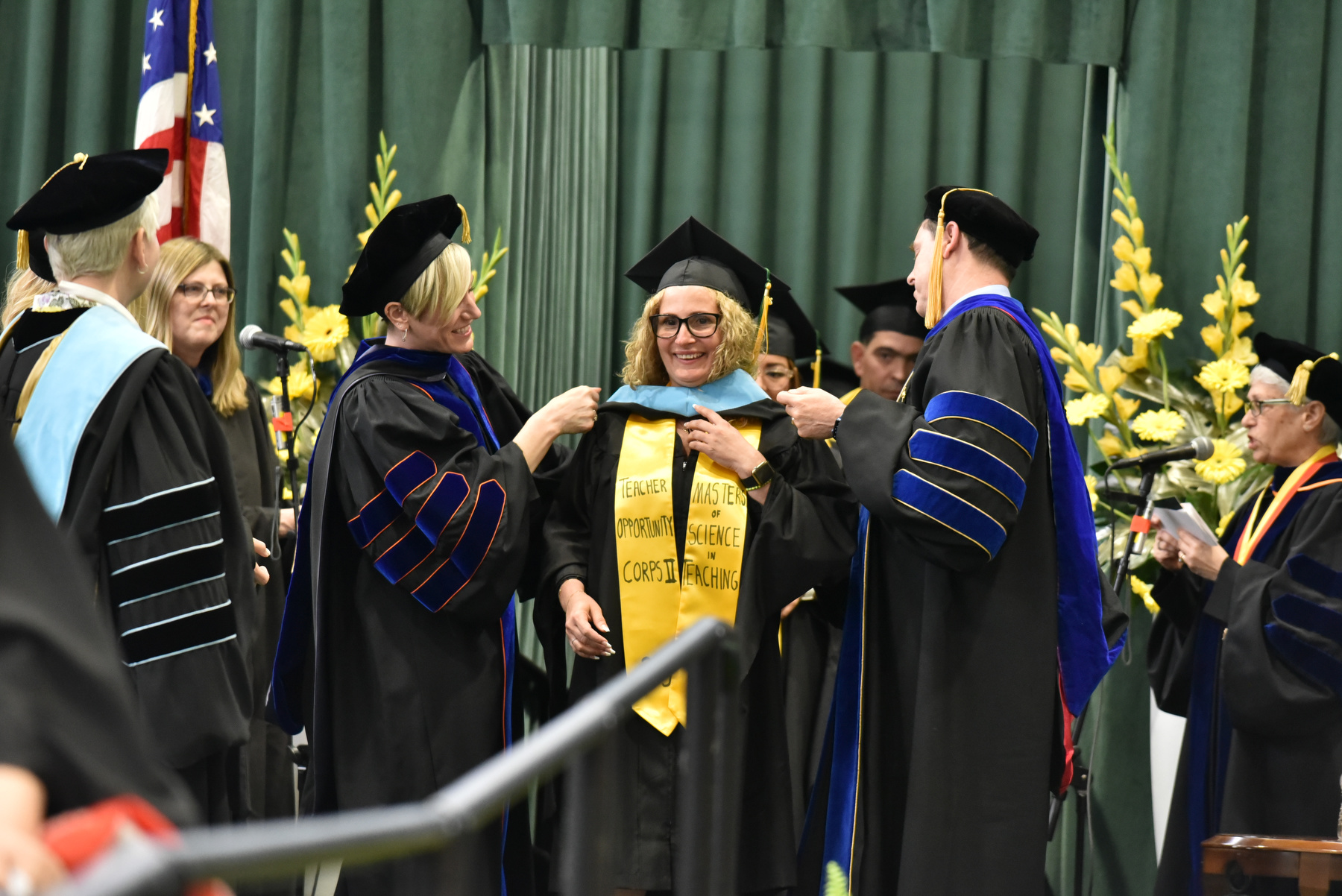 Master’s degree candidates are bestowed with their hoods on the platform during the School of Education commencement by Dean of Education Laura Spenceley and Provost Scott Furlong.
