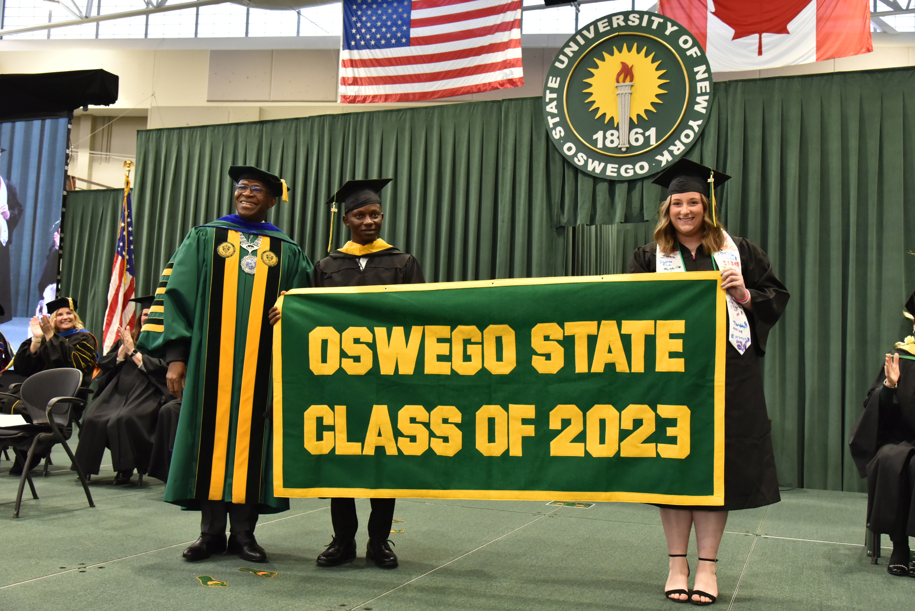 One of the high points at Commencement is the presentation of the alumni banner officially welcoming all of the new graduates into the Oswego Alumni Association. President Peter O. Nwosu stands with Otis Gbala, who earned a master’s in biomedical and health informatics, and Kaleigh Janes, who earned a bachelor’s in electrical and computer engineering, while they display the banner on the platform.