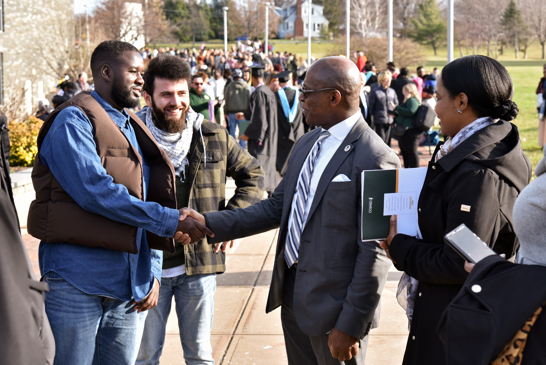 Families, friends and alumni gather outside the Marano Campus Center after the Dec. 16 Commencement ceremony on a relatively warm and sunny day. Pictured, President Peter O. Nwosu greets Yahya Ndiaye, a 2022 graduate in Oswego's electrical and computer engineering program, and other visiting alumni and supporters.