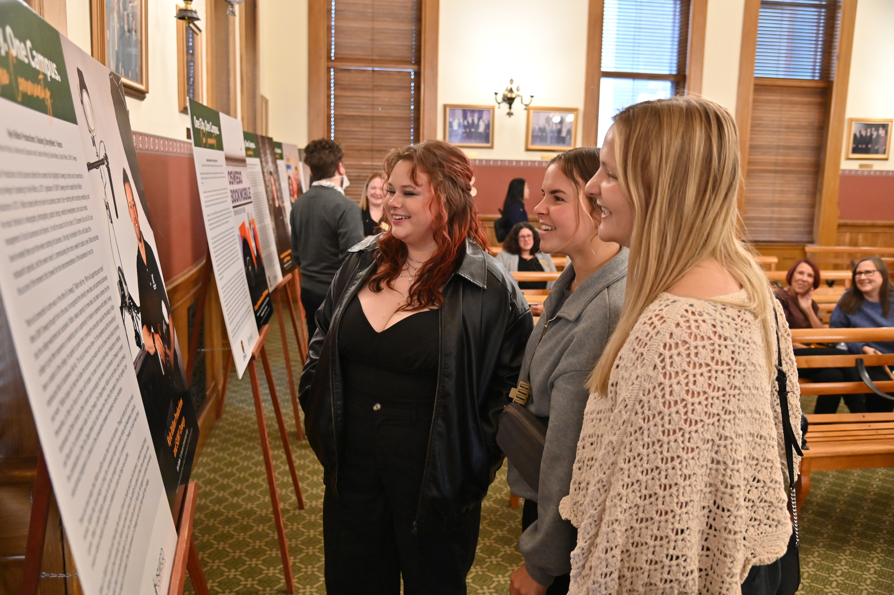 Emma Gabriel (left), a studio art major with an arts management and photography double minor, talks with friends about her work on display at Oswego City Hall included in the One City. One Campus. One Community. photojournalism project.