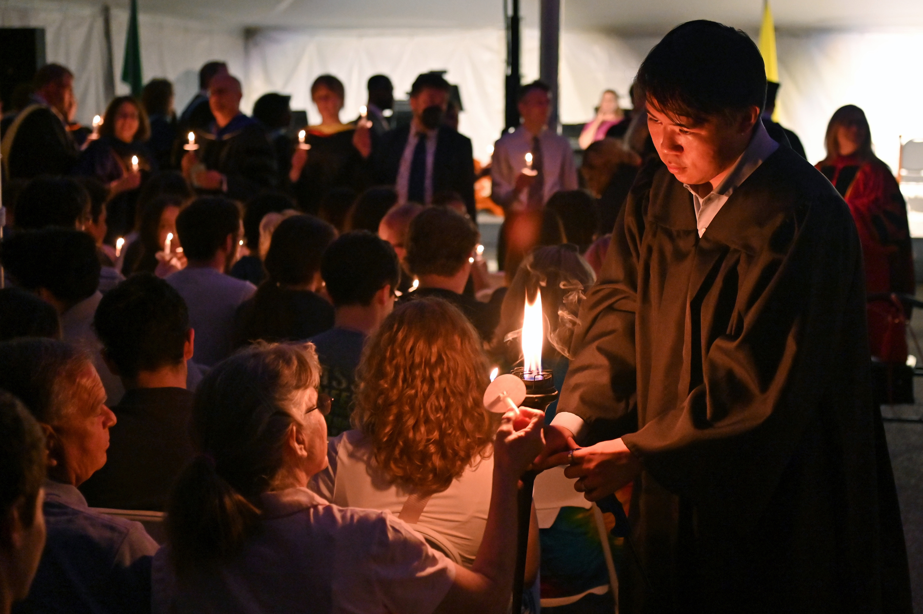 Torchbearer Shaun Lin ’25 passes the ceremonial flame to candles held by graduating seniors, their families, friends and other audience members during the Commencement Eve Torchlight Ceremony on May 16.