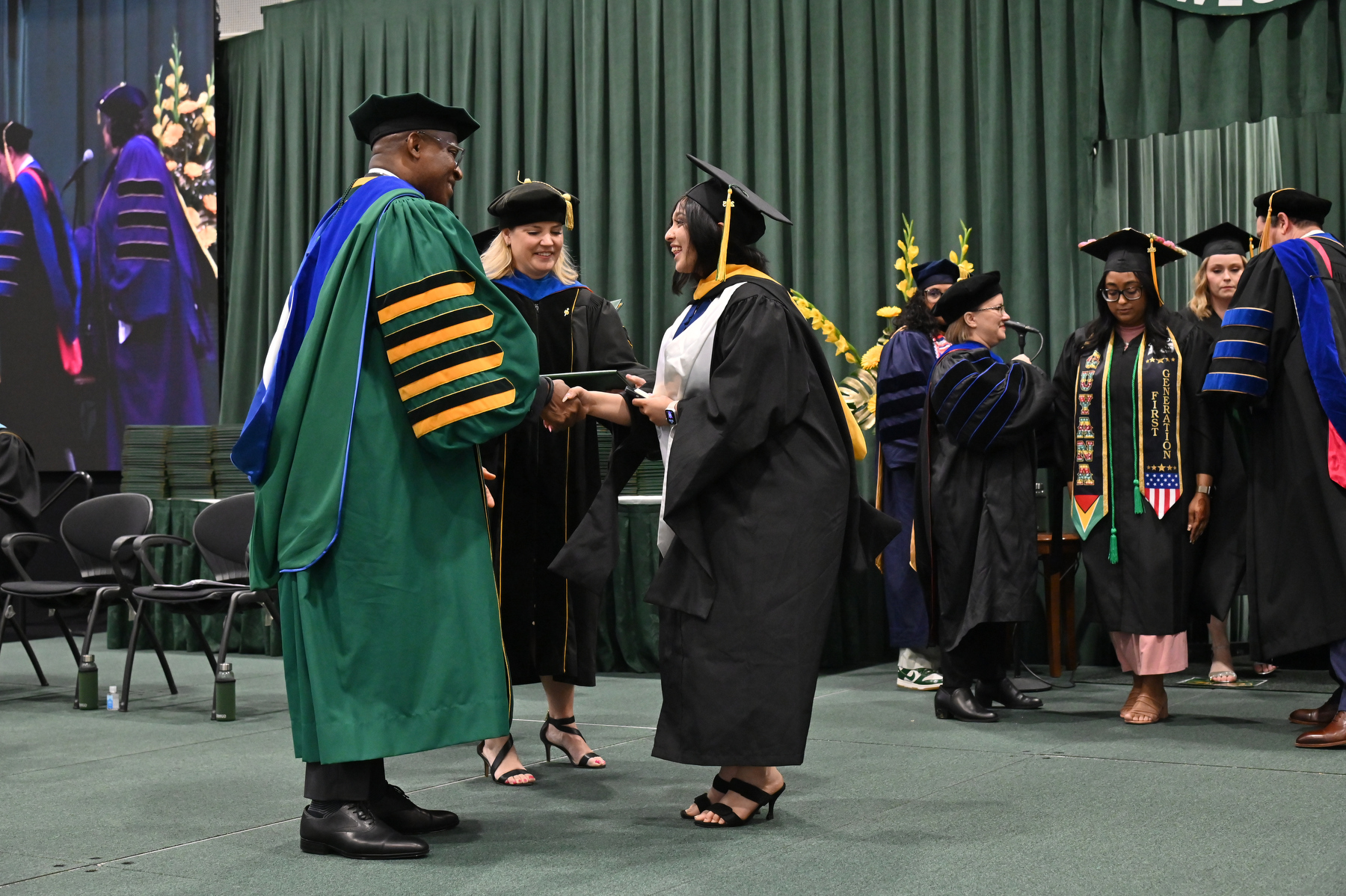 Graduates shake hands with their deans and President Peter O. Nwosu as each is recognized as they walk across the platform.