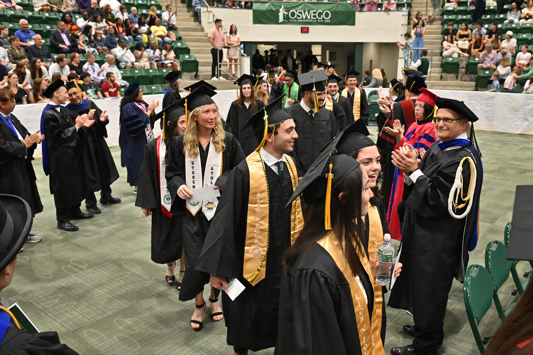 Graduates in the School of Business enter the hall prior to the 12:30 p.m. ceremony to the applause from faculty in the floor, and guests in the arena.