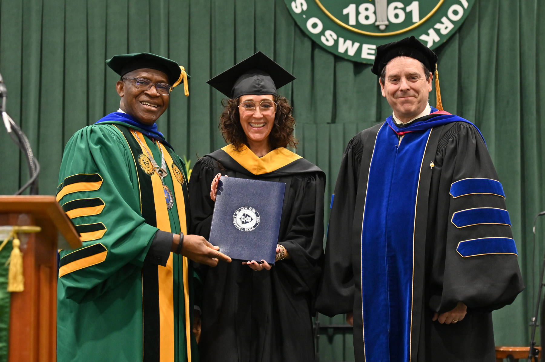 Constance Schwartz-Morini of the Class of 1990, the co-founder and CEO of highly successful SMAC Entertainment, is presented with the honorary doctor in humane letters degree during the School of Business ceremony by President Peter O. Nwosu and Scott Furlong, provost and vice president for academic affairs.