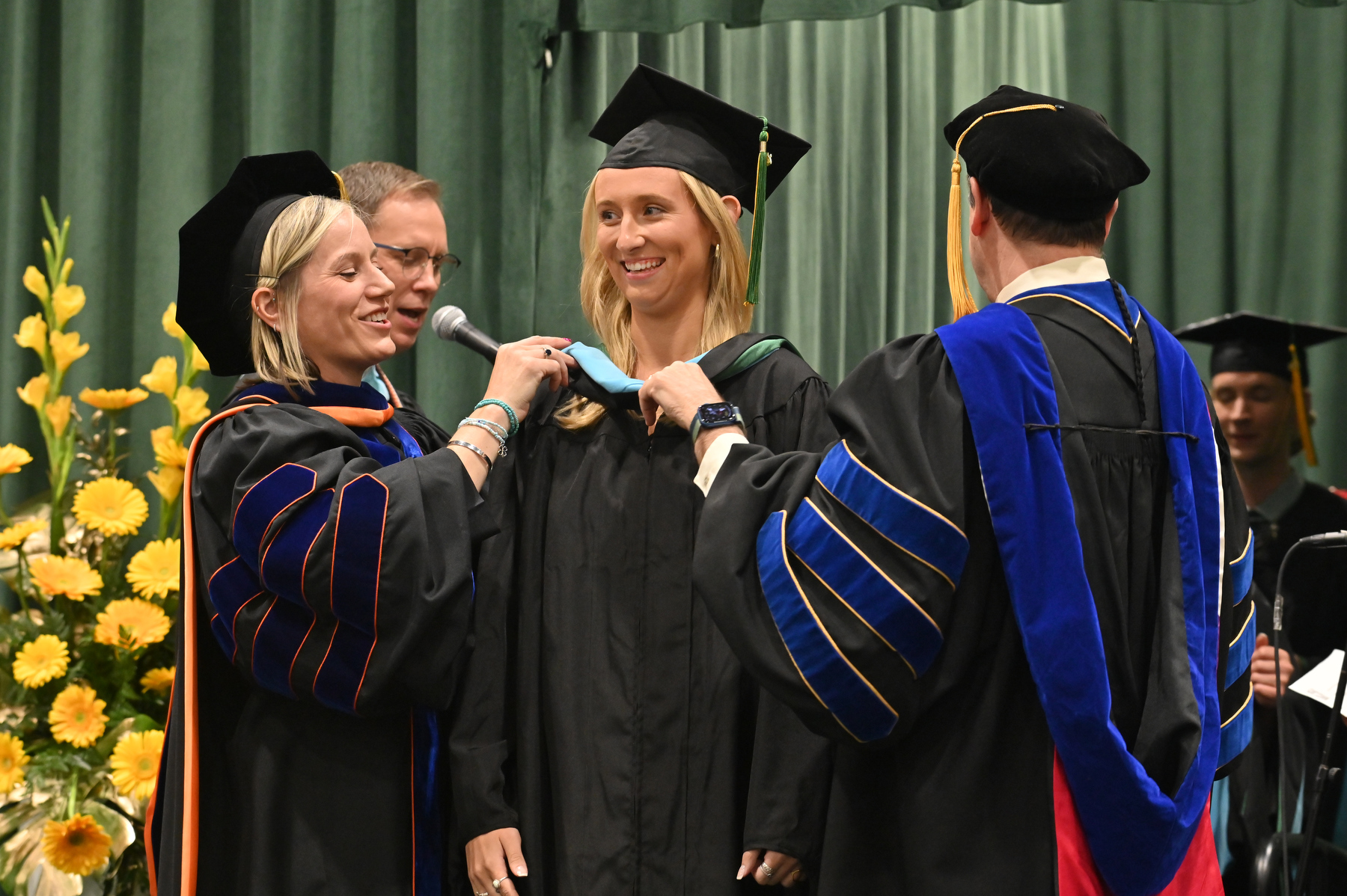 Master's in education graduates are hooded on the platform by Laura Spenceley, dean for the School of Education, and Scott Furlong, provost and vice president for academic affairs.