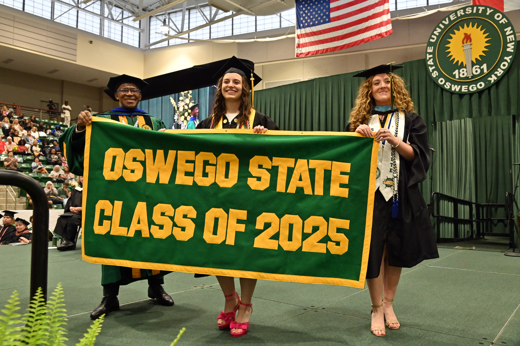 Melinda Brancato and Bryleigh Beauchat present the Class of 2025 Alumni Banner to President Peter O. Nwosu at the ceremony for the School of Communication, Media and the Arts and the School of Education.