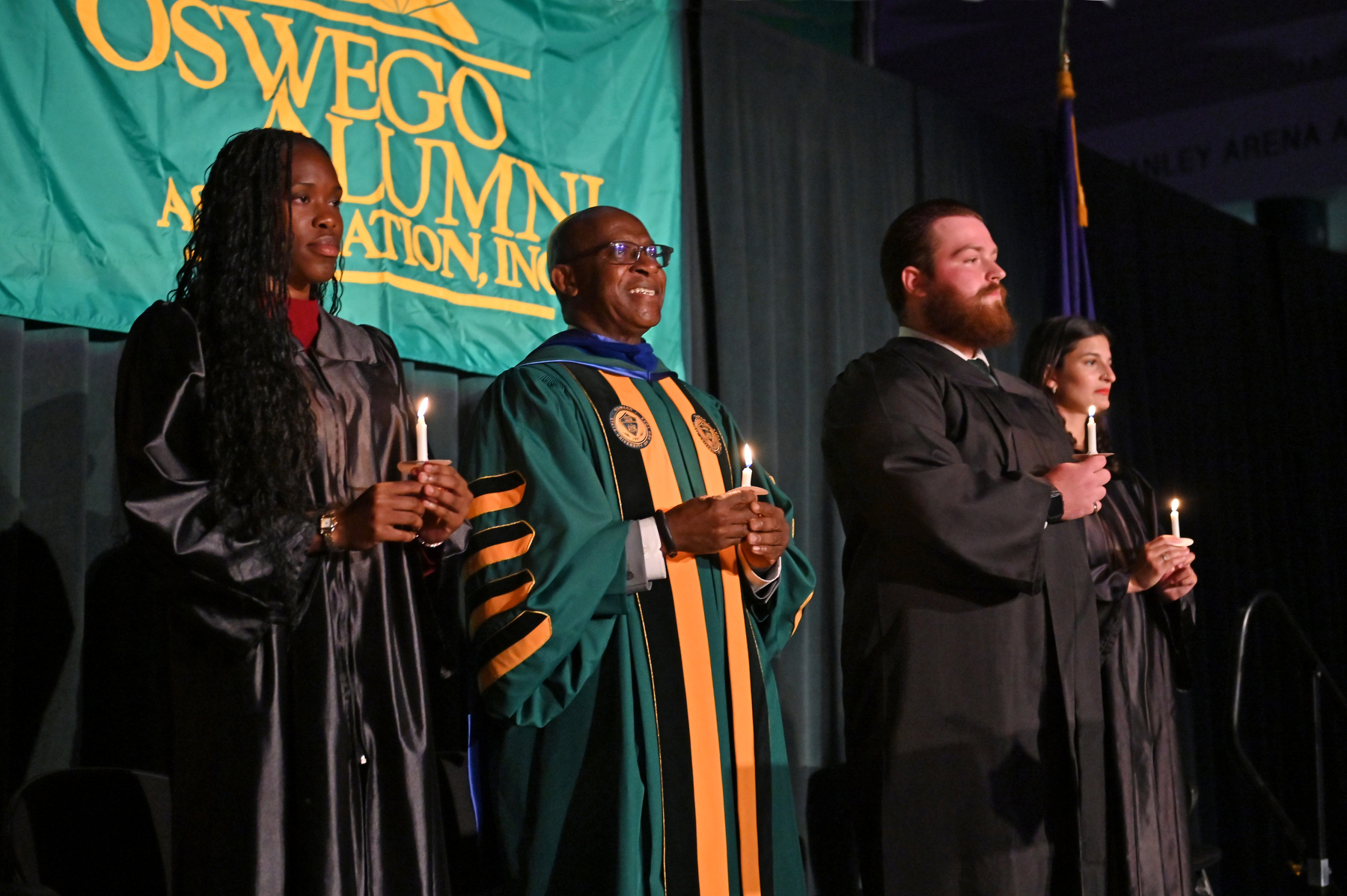 At the Welcoming Torchlight Ceremony, President Peter O. Nwosu stands on the platform with, from left, torchbearer Oghenetega “Tega” Adjoh ’26, student emcee Kenneth “Kenny” Girard ’26 and student speaker Alexandra “Alex” Teitelbaum ’26.
