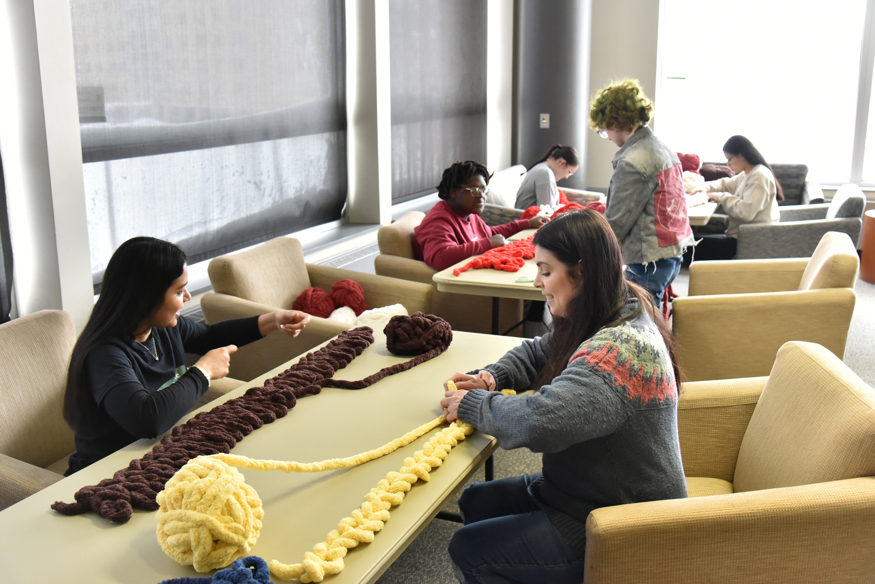 As part of the Feb. 7 in the Martin Luther King Jr. 2026 Day of Service, Jacqueline Wallace (seated right), associate director for career education in Career Services, works with students in the Hearth Lounge in Marano Campus Center making hand-knitted blankets.