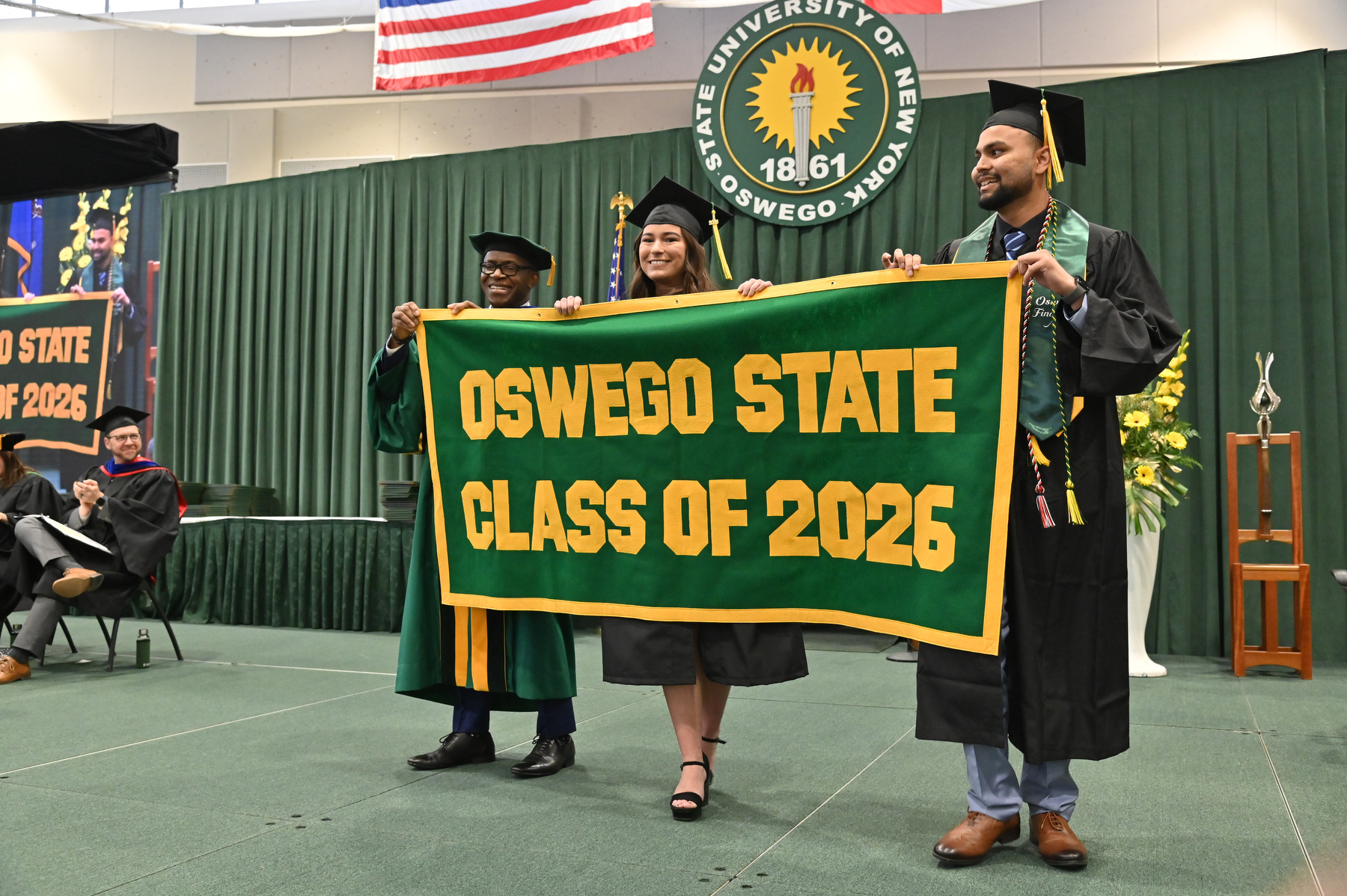 Brooke Holzlein and Meet Patel present the Class of 2026 Alumni Banner to President Peter O. Nwosu on the commencement platform during the 12:30 p.m. ceremony for the College of Business and Entrepreneurship. 